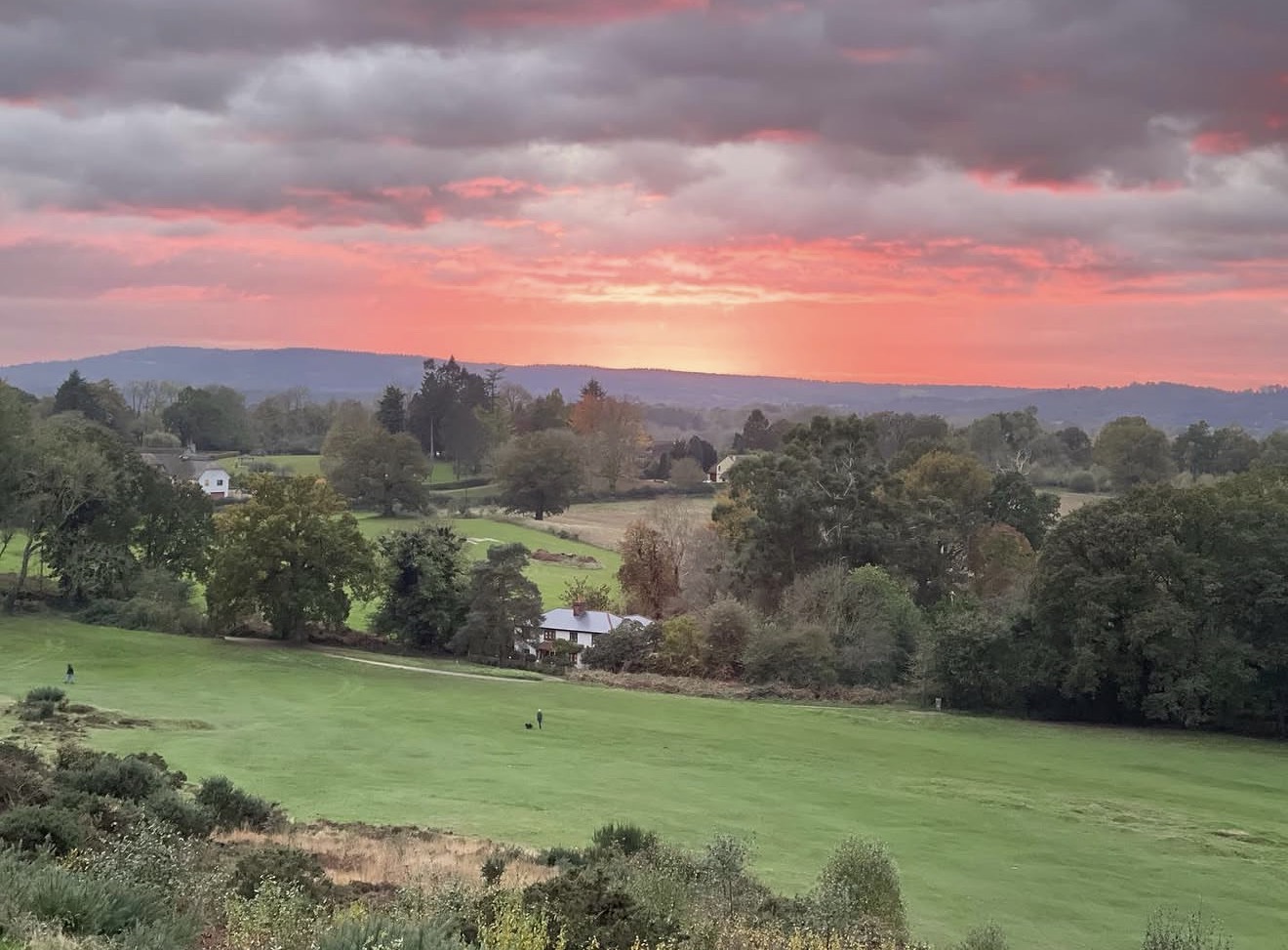 Pink and golden sunset over the golf course, trees and distant hills at Reigate Heath